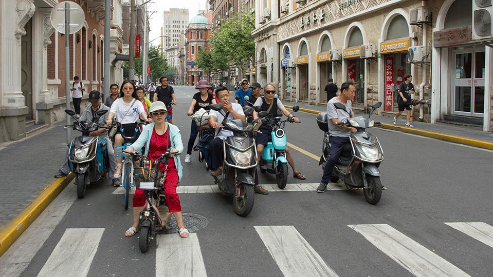 Sieben Elektro- und Motorroller stehen an Fussgängerstreifen in Shanghai