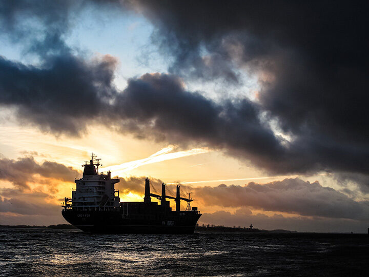 Ein Frachtschiff bei Sonnenuntergang und dunklen Wolken am Himmel