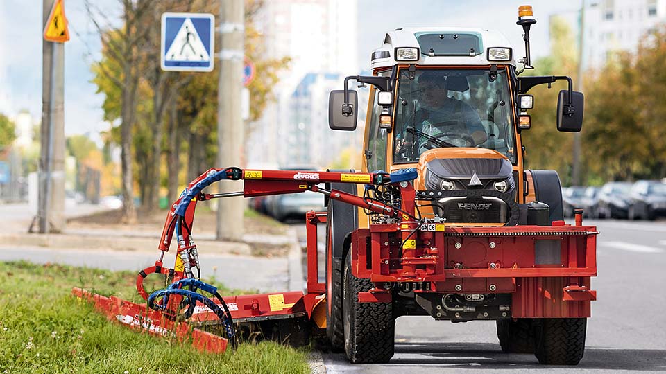 Oranger Traktor mäht Gras in der Stadt