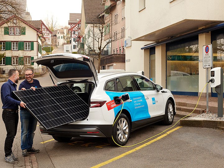 Zwei Personen verladen ein Solarpanel in ein E-Auto mit Firmenbeschriftung