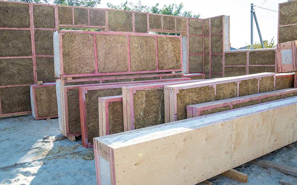 Mit Stroh gefüllte Holzrahmen bilden eine Wand, weitere Hybridelemente stehen zur Montage bereit
