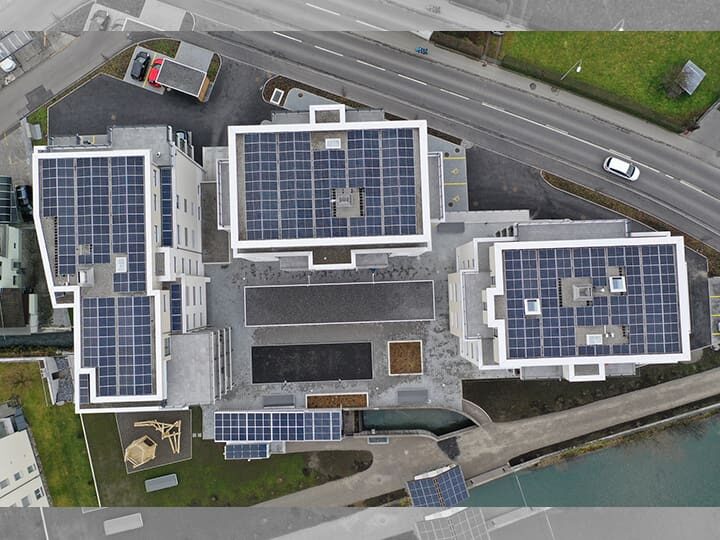 Luftbild eines Areals mit drei grossen und mehreren kleinen Gebäuden, deren Dächer alle mit Photovoltaikpanels belegt sind